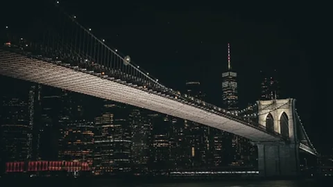 New York Brooklyn Bridge. El puente de Brooklyn iluminado se extiende ante el horizonte nocturno de Nueva York. La oscura escena urbana aporta profundidad a los espacios de trabajo modernos.